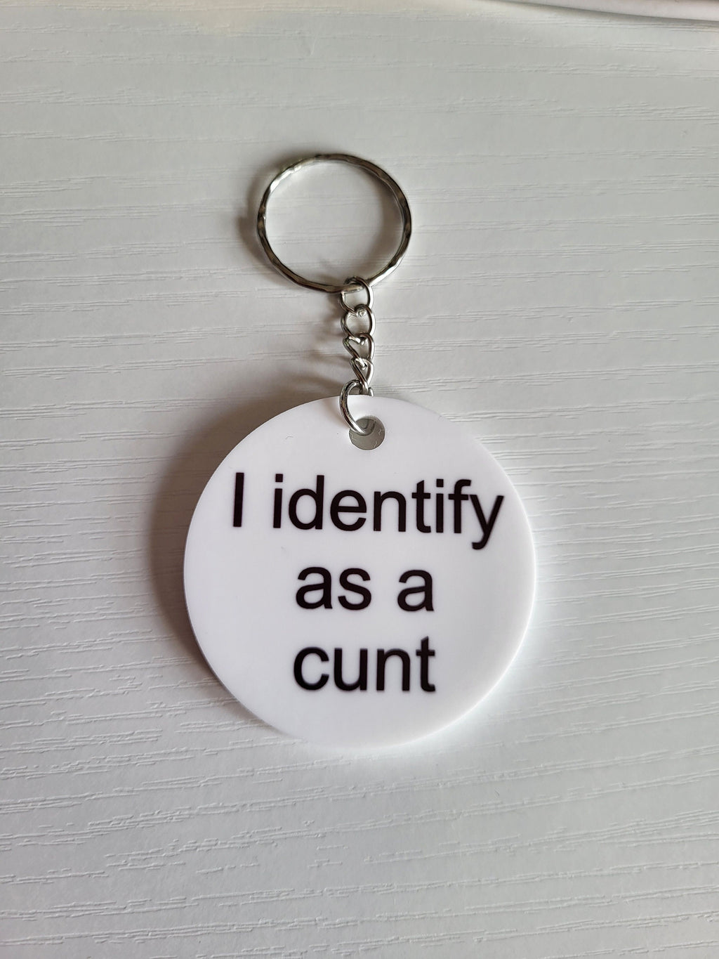 White keychain with controversial message. Silver keyring on a textured white surface.