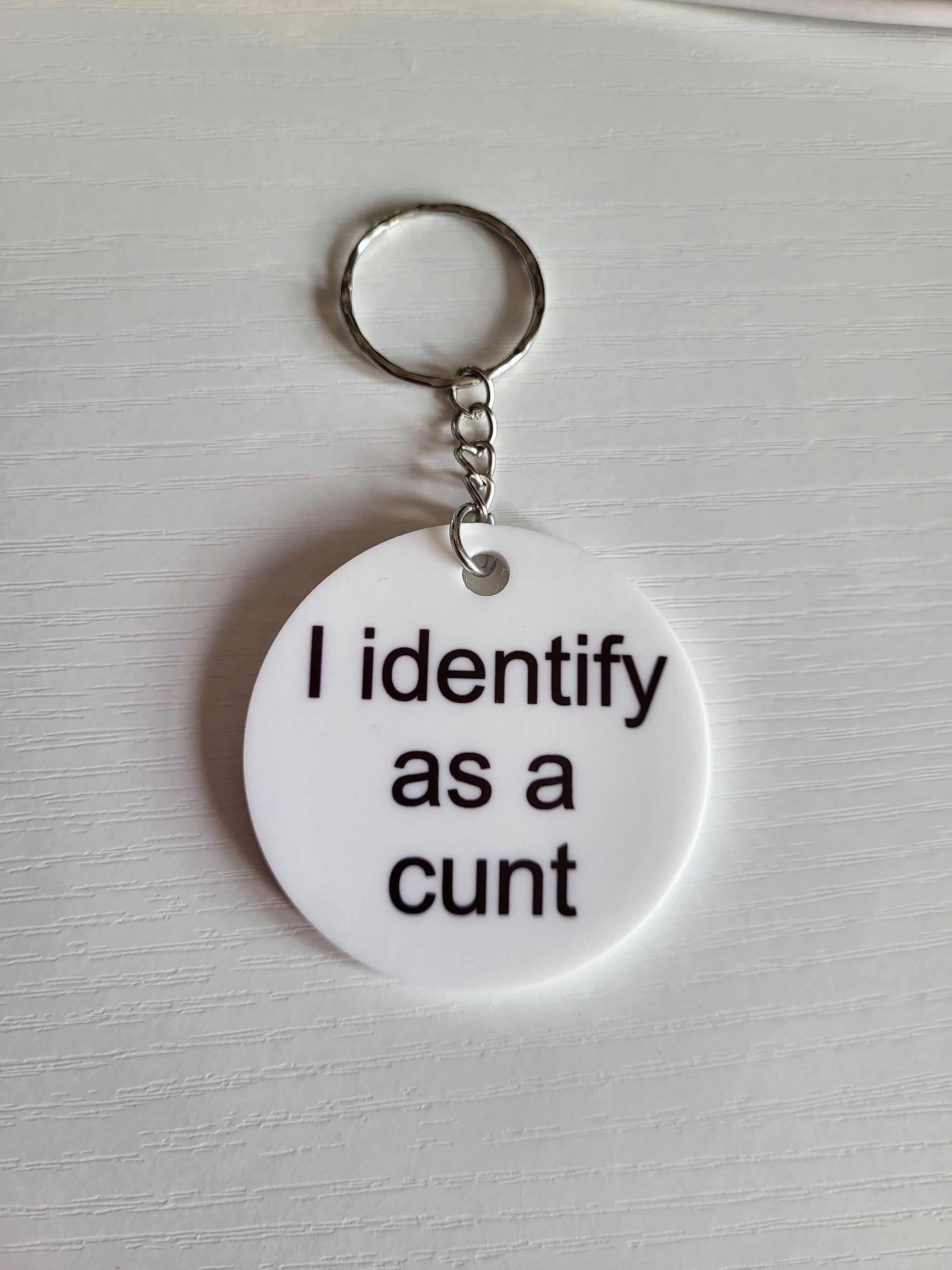 White keychain with controversial message. Silver keyring on a textured white surface.